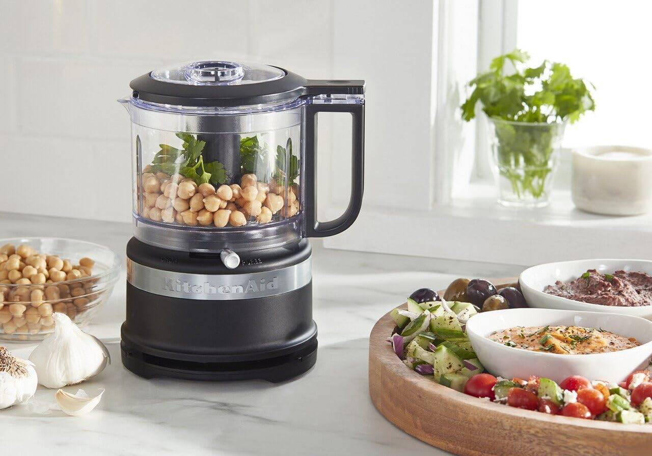 A small food processor on a counter with some chickpeas inside, making hummus.