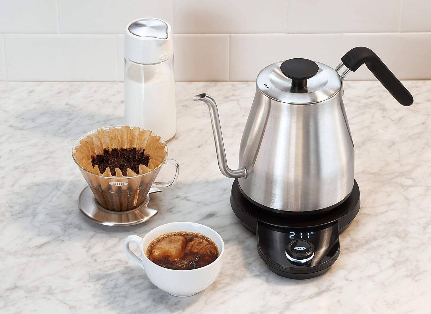 A gooseneck electric kettle on a counter next to a cup of coffee, pourover, and water bottle.