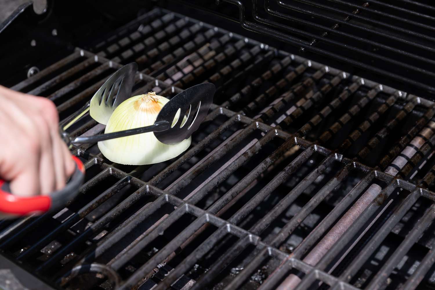 Someone cleaning a grill with an onion being held by tongs.