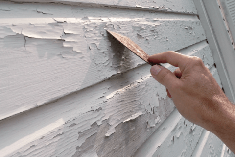Scraping peeling paint off the exterior of a house.