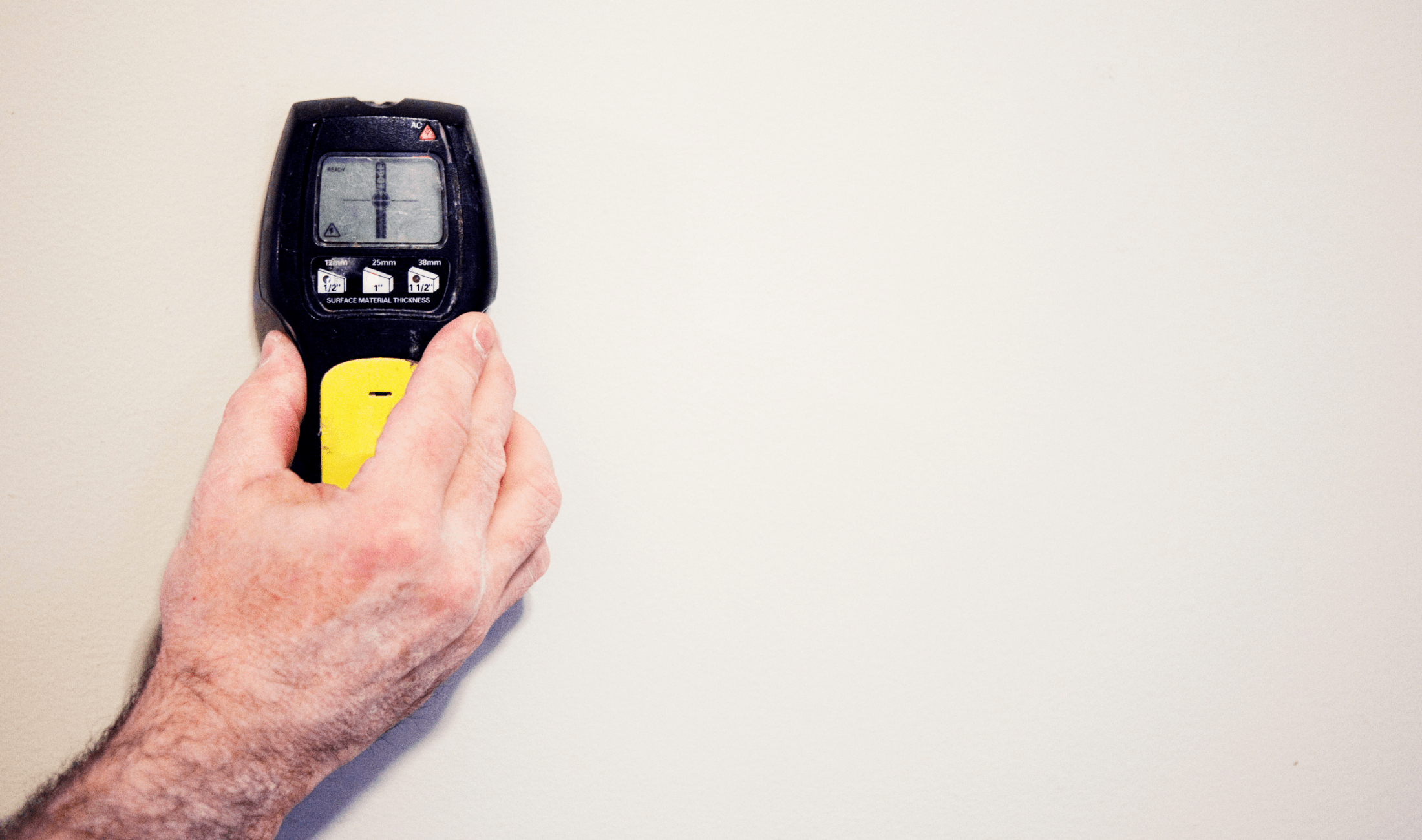 A hand holding a stud finder against a wall.