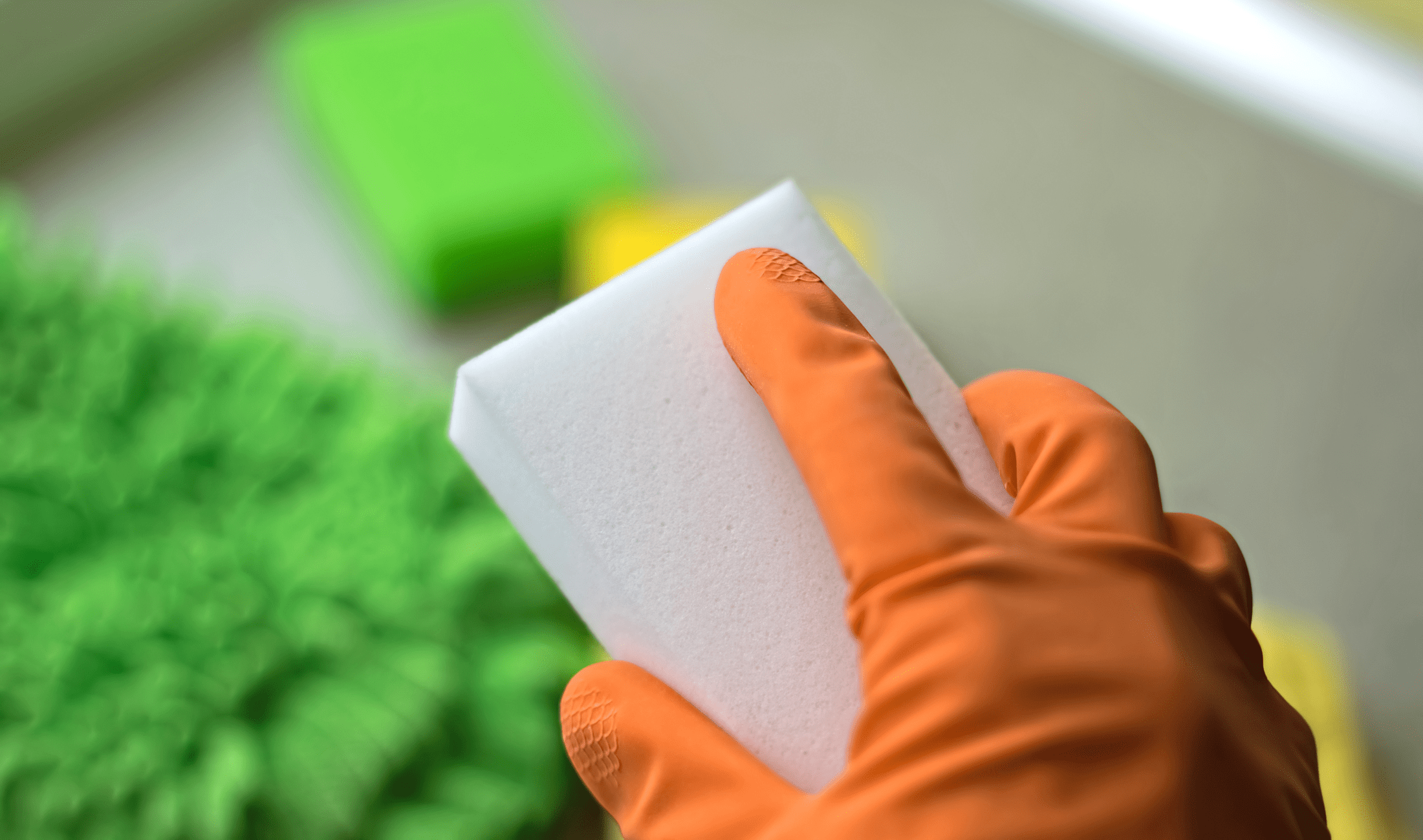 An orange-gloved hand holding a melamine sponge.
