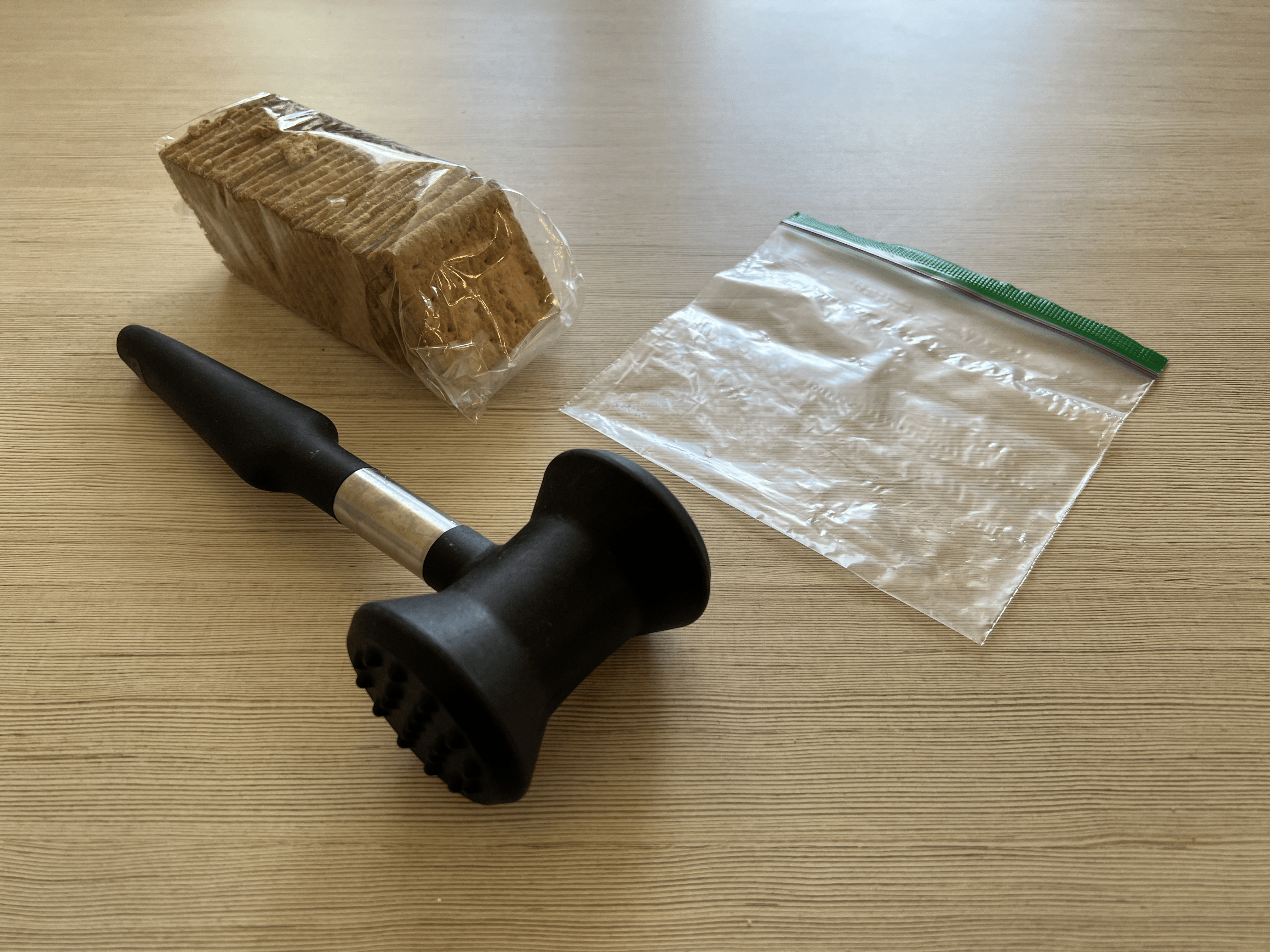 A mallet, sleeve of graham crackers, and a ziploc bag all on a table.