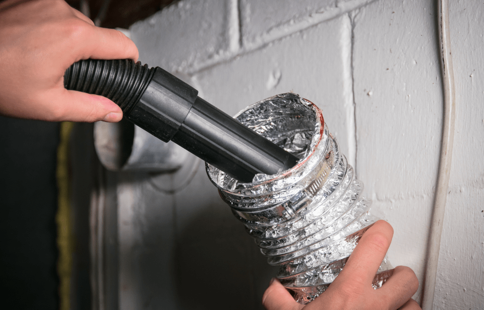 A hand holding a vaccuum that's cleaning the inside of a dryer hose.